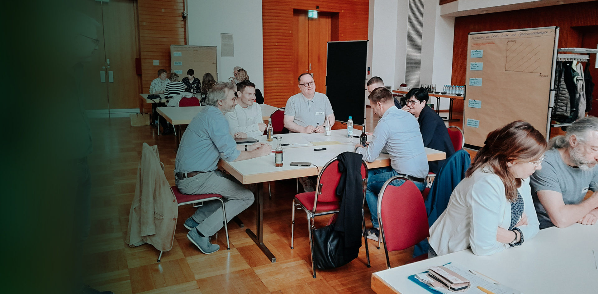 Bürgerforum zum Maßnahmenkatalog der Leipziger Zero-Waste-Strategie am 11. November 2023. Personengruppen sitzen in einem großen Raum an verschiedenen Tischen und unterhalten sich angeregt. Im Hintergrund große Flipcharts und Tafeln mit handschriftlichen Skizzen und Notizen.